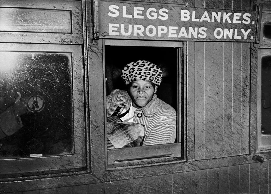 אשה שחורה יושבת במחאה בקרון רכבת שנכתב עליו 'לבנים בלבד. אירופאים בלבד'. דרום אפריקה, 1952