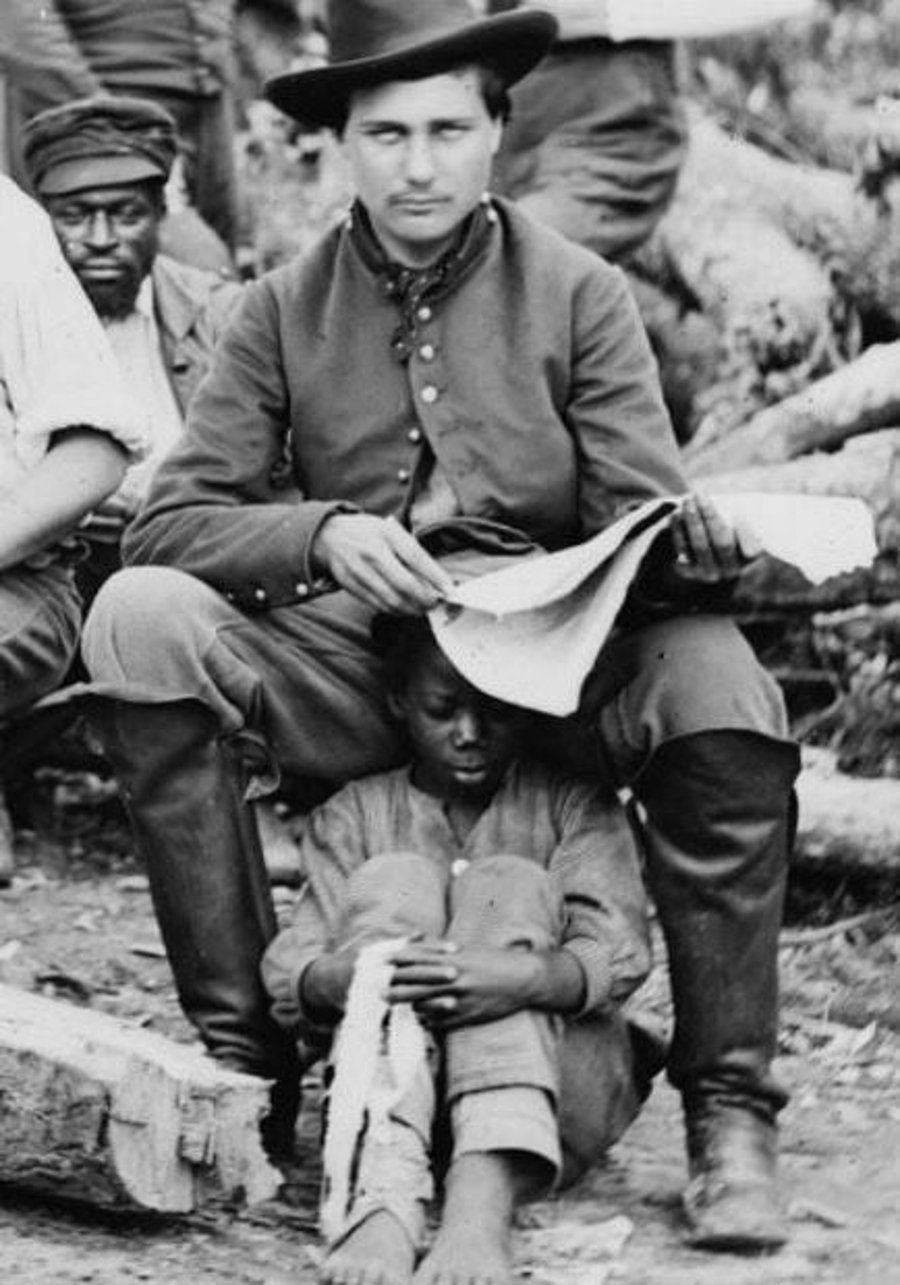 קצין בכוחות הקונפדרציה משתמש בילד כהה עור, עבד משוחרר, ככיסא. ארה"ב 1862