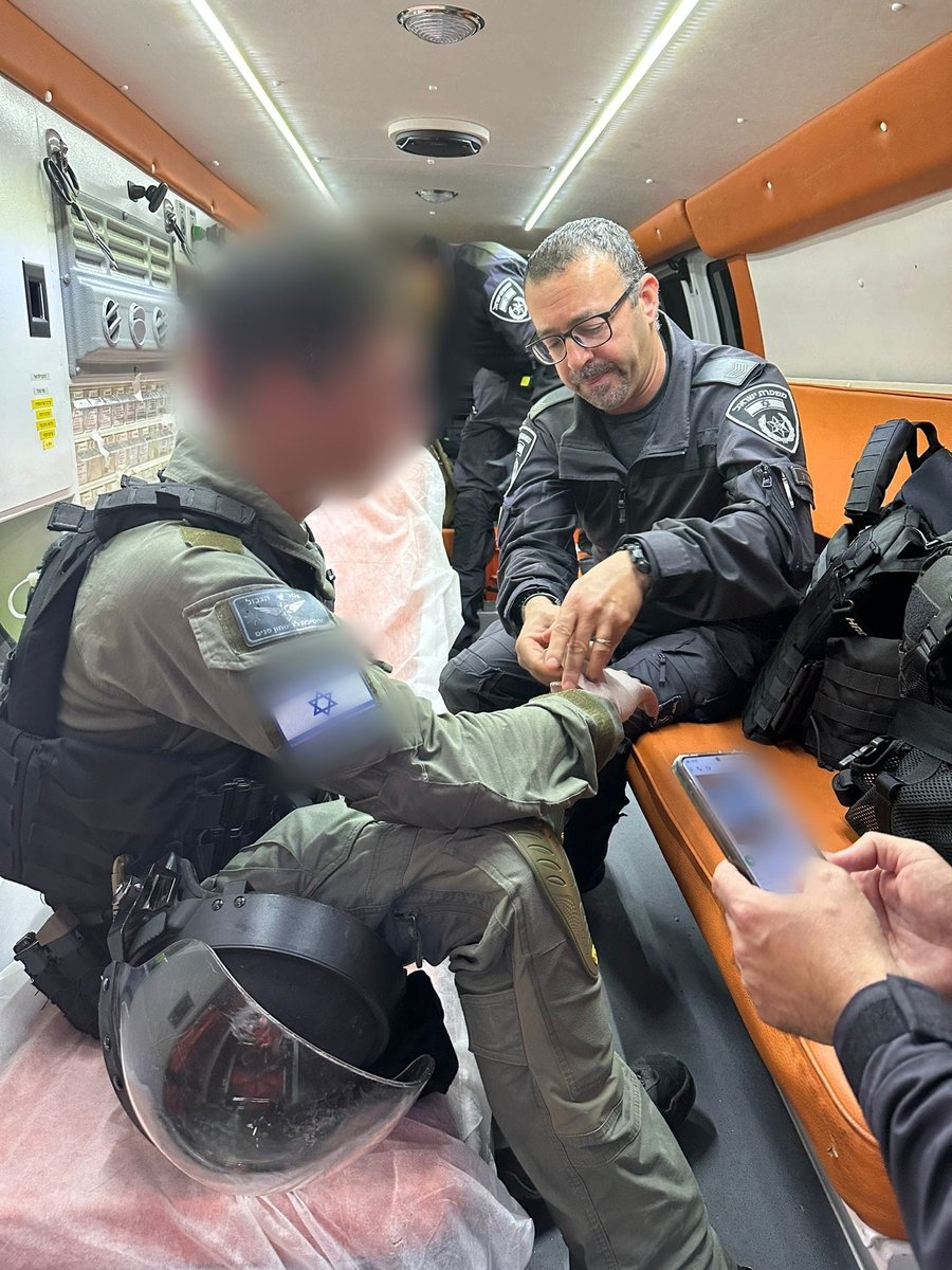 שוטרים שמים פלסטר בתוך ניידת אמבולנס על ידו של שוטר שנפצע מאלימות המתפללים